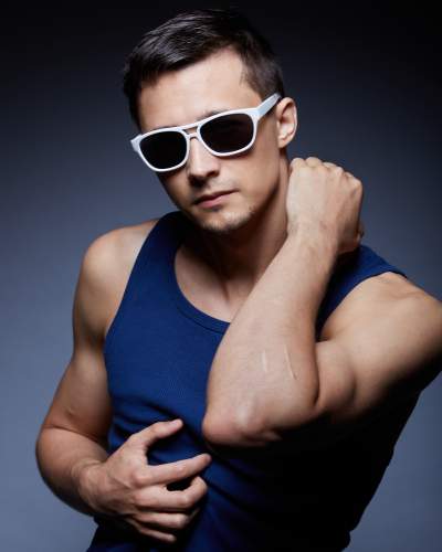 Man in a navy blue Aussiebum tank top and white sunglasses posing confidently with a stylish, intense expression.