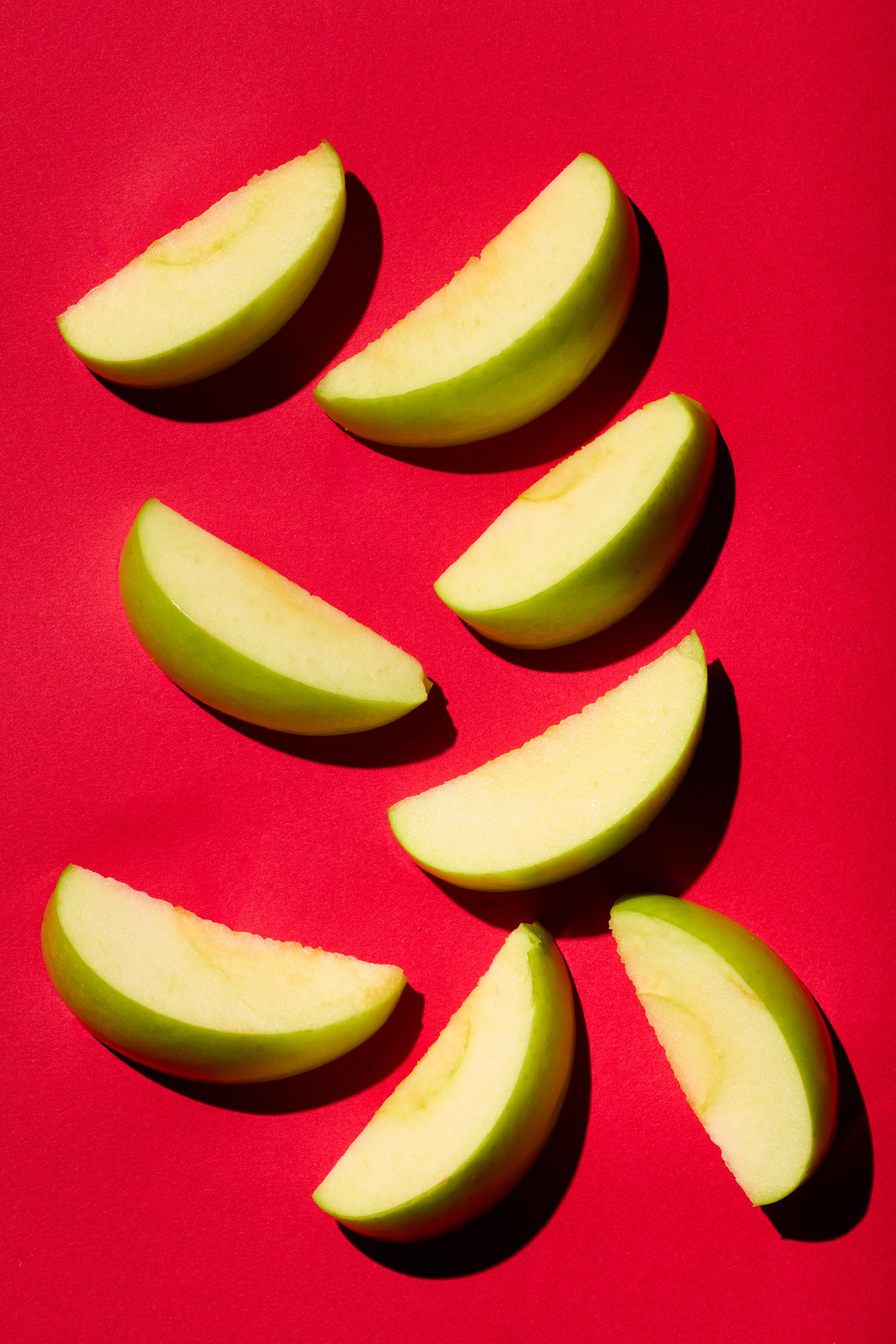 Slices of green apple arranged on a vibrant red background, with strong shadows creating a bold and modern composition.