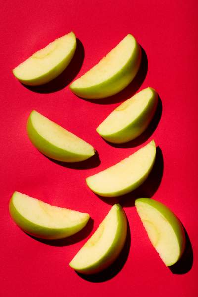 Slices of green apple arranged on a vibrant red background, with strong shadows creating a bold and modern composition.
