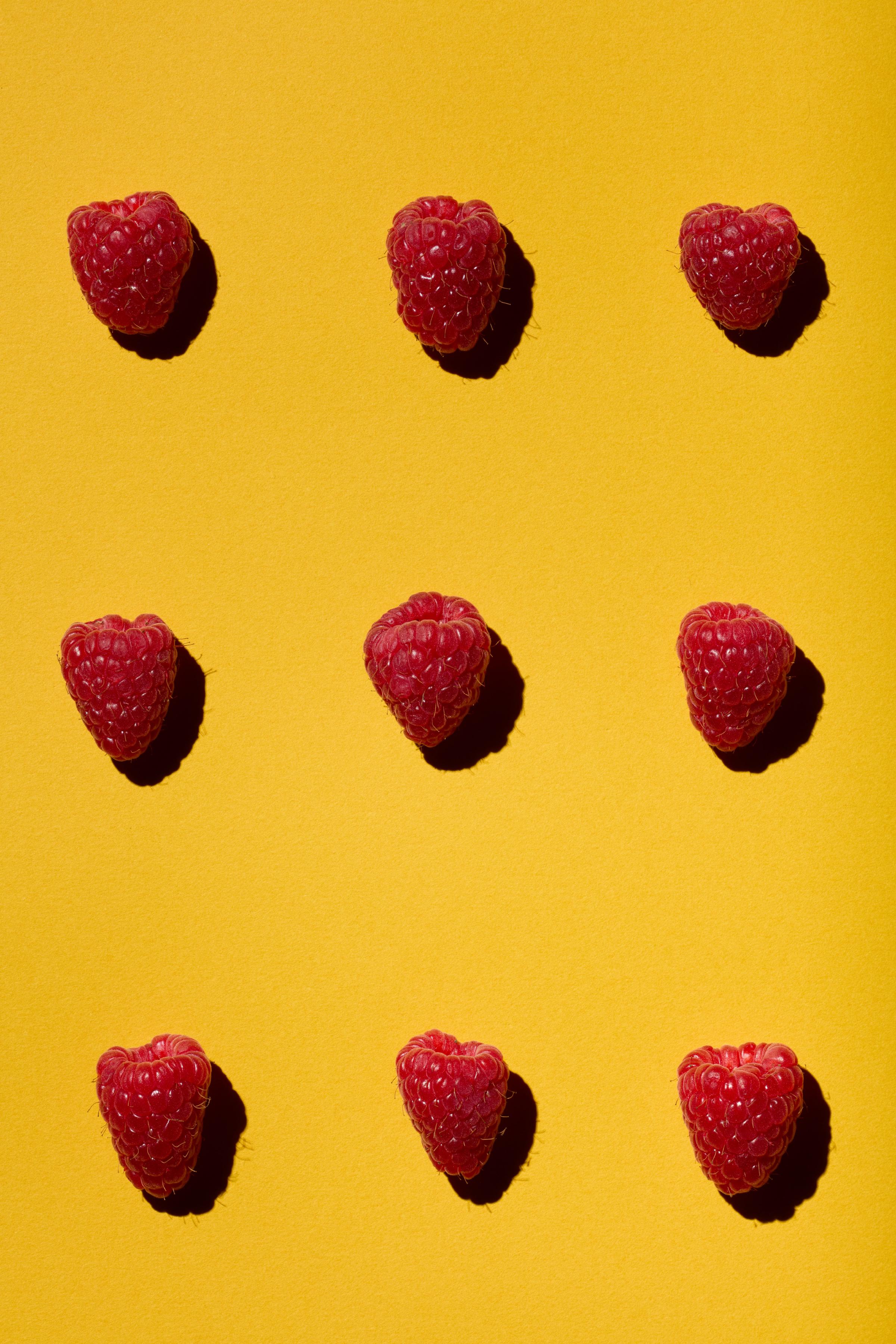 Nine fresh raspberries evenly arranged on a vibrant yellow background.