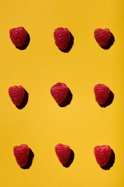 Nine fresh raspberries evenly arranged on a vibrant yellow background.