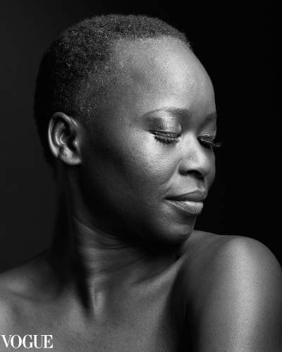 Black and white portrait of a woman with short natural hair, her eyes closed and head tilted gracefully to the side, showcasing her serene expression and smooth skin, with Vogue branding in the corner.